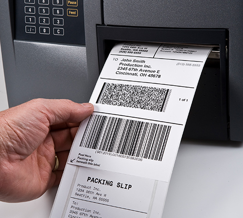 A hand pulling integrated shipping labels out of a printer.