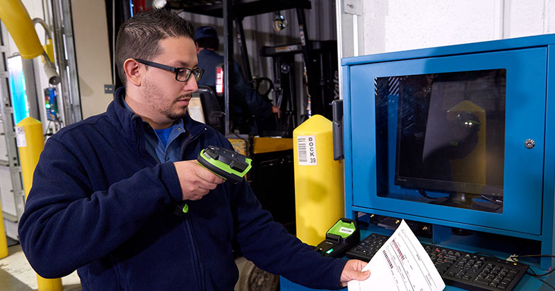 A warehouse worker is scanning a paper document with a Zebra ultra-rugged barcode scanner.